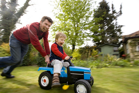 推孩子车素材一种乐趣背部父亲把他儿子推在玩具拖拉机上在他们后面的花园主题振奋家庭团结里背景