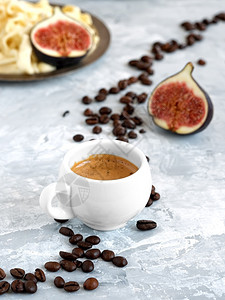 满就返白杯子灰色背景上有新鲜酿制的浓咖啡烤豆就放在一杯咖啡旁背景是鲜红无花果和自制芝士白色的起司早晨背景