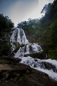 旅行后部自然的瀑布从悬崖流下长的一条线从悬崖流到微小的山谷湖图片