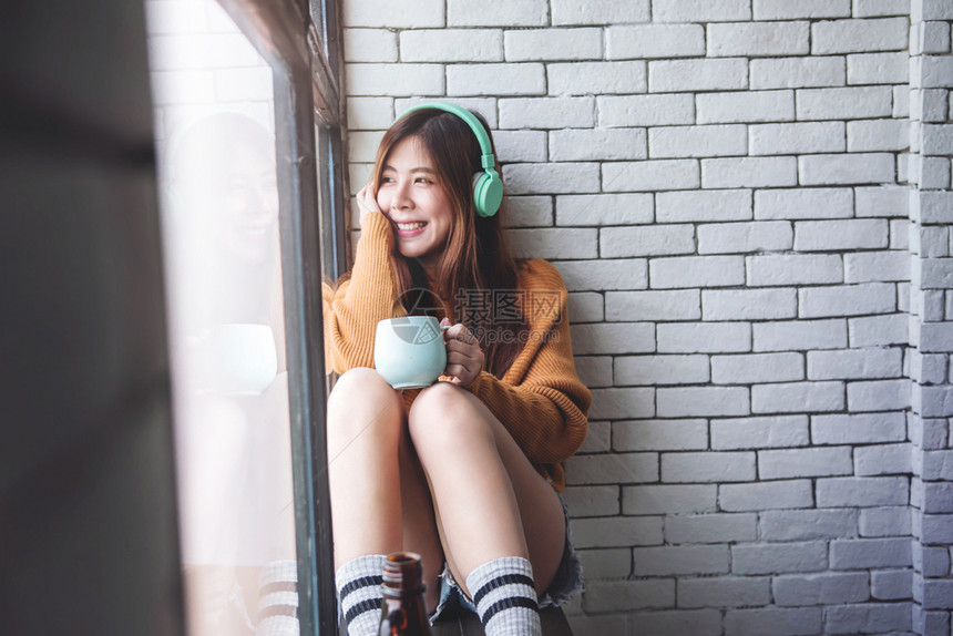 潮人快乐的年轻女软焦点在靠近窗户的CozyHouse中从耳机开始放松音乐享受阳光和热咖啡的早晨美丽图片
