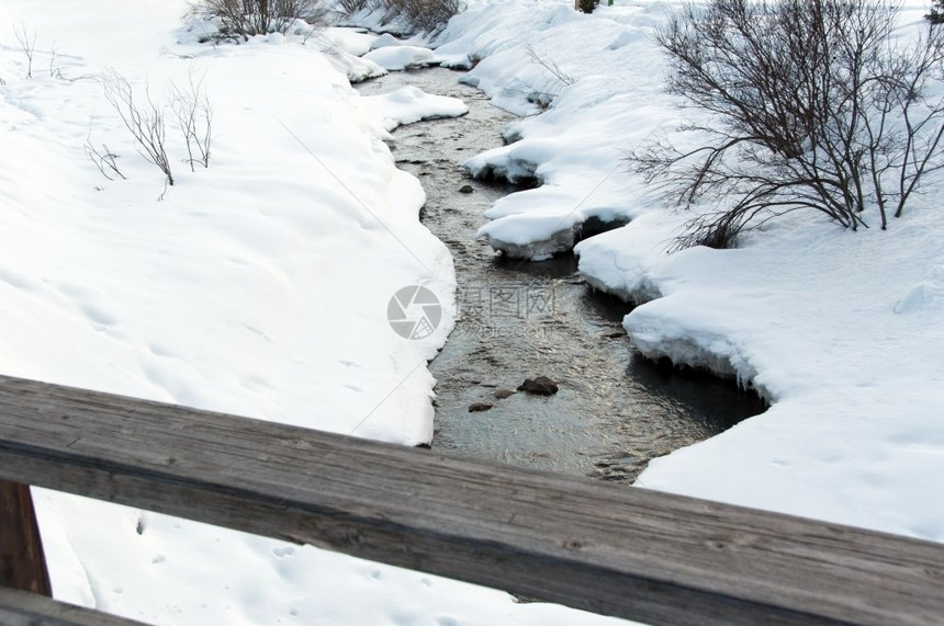 高德纳冰柱霜溪流穿过雪覆盖的河岸和一座桥木铁轨图片