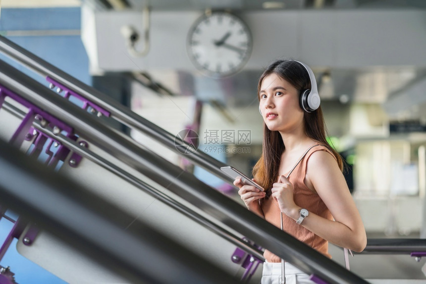 爆发轻轨年亚洲女乘客在大城市通勤和交上旅行时佩戴耳机和使用智能移动电话聆听音乐并走在地铁站的楼梯上如乘坐大城市往返车和交通商业图片