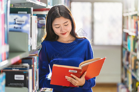 站在图书馆书架旁认真阅读书籍的女孩背景图片