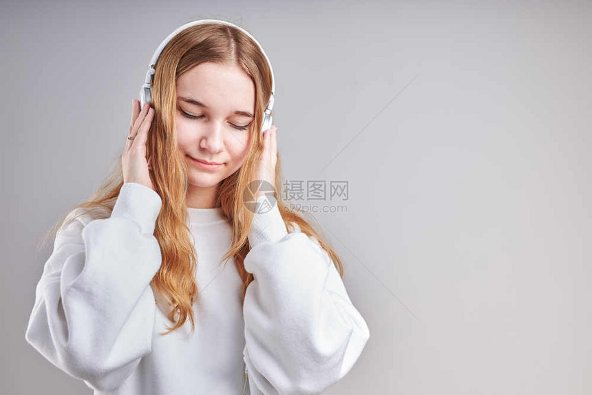 可爱的超过微笑年轻女孩聆听音乐流内容于观看视频享受聊天与朋友使用智能耳机对面做手势表情的交谈坐在浅灰色背景上的耳机图片