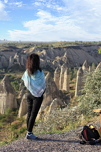 砂岩户外肩膀一只年轻女孩站在悬崖边缘看着山峰峡谷和卡帕多西亚的蓝天空一个年轻女孩站在悬崖边缘看着地平线卡帕多西亚山谷和蓝天Cap背景图片