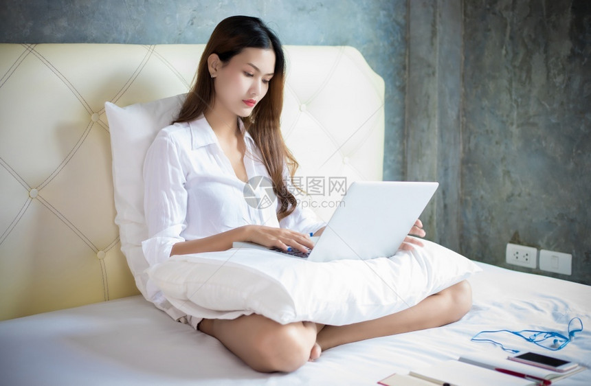 微笑互联网亚洲妇女在家里工作时使用笔记本电脑她坐在床上科罗纳流行期间被隔离日冕的流行图片