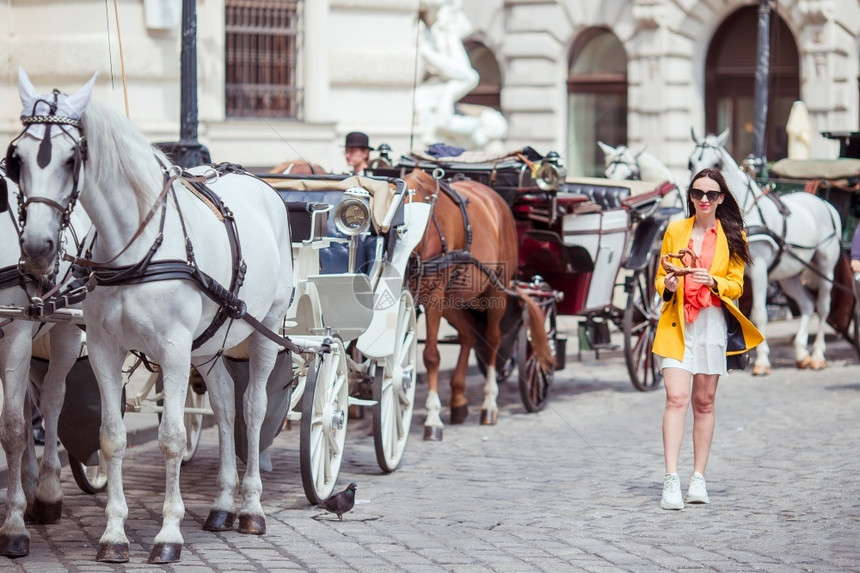快乐的女子在欧佩安街上行走年轻有吸引力的旅游者在维也纳市的露天游览在广场旁的维也纳市一辆载有两匹马的车骑着女人在城里行走一种镇在图片