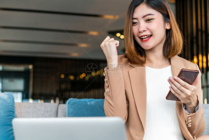 商界女亚洲企业家在通过现代办公室或合用空间的技术笔记本电脑和移动话技术资金钱包和在线支付概念检查成功目标时庆祝亚洲女商人们的节日图片