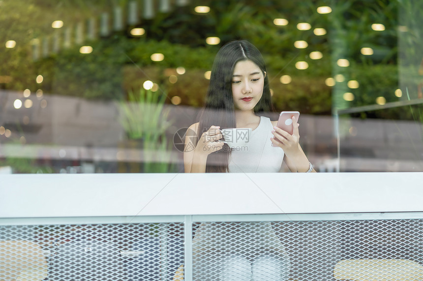 亚洲年轻女在现代咖啡店或工作间使用手机与窗户镜子技术智能移动和潮时生活方式企业家概念等相邻的窗口镜智能移动和时装生活方式以及创业图片