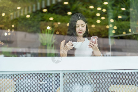 亚洲年轻女在现代咖啡店或工作间使用手机与窗户镜子技术智能移动和潮时生活方式企业家概念等相邻的窗口镜智能移动和时装生活方式以及创业背景图片