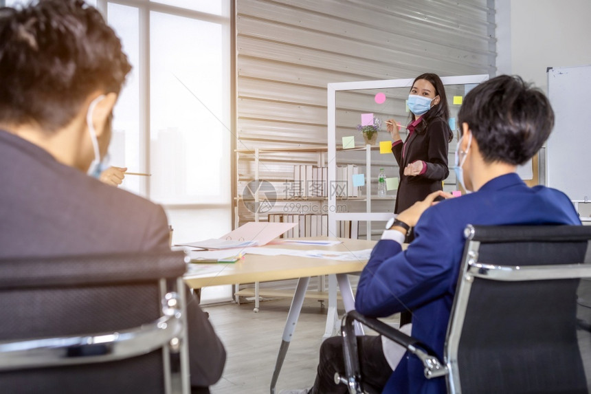 沟通房间亚洲身戴保护面罩着的亚裔女商业妇使用保护面罩在办公室CCOVID19会议室玻璃墙上分享防暴思想概念时指出图片