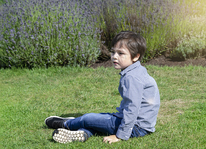 衬套家庭有选择焦点小男孩面带微笑的脸坐在草地上露天菜鸟田里的草地上快乐孩子肖像在户外玩耍有着模糊的鲜花背景公园图片