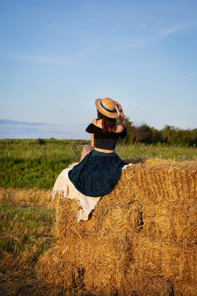 场地农业户外戴草帽的年轻美女看着夕阳孩坐在一大堆草捆上温暖的夏夜戴草帽年轻美女看着夕阳孩坐在一大堆草捆上温暖夏夜图片