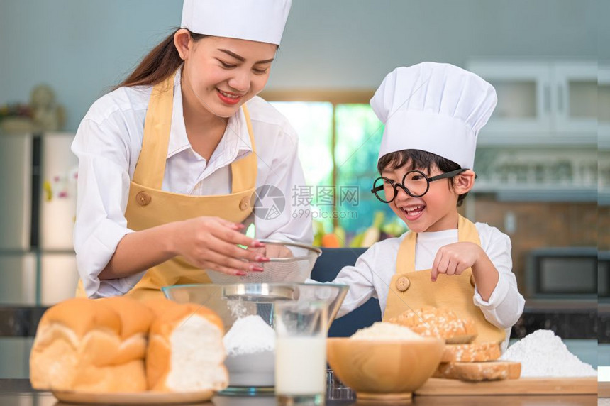 桌子可爱的亚洲小男孩和美丽的母亲在餐桌上的厨房里用筛选器把面粉擦成里有筛子细水沟在厨房里准备烘烤面包店和蛋糕女儿亚洲人图片