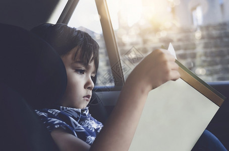 只跑一次假期喜悦小孩坐在车座上阅读一本书小男孩坐在儿童安全座位上的汽车里幼童肖像在一次公路旅行中给头儿们送餐用车和孩子一起玩弄安全概念亚背景
