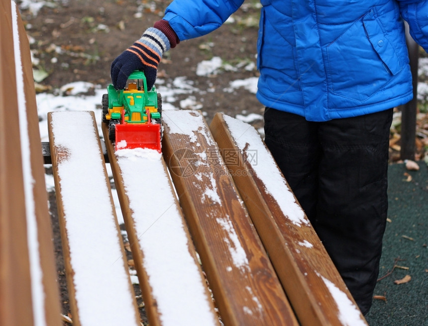 熔化自然一个小孩站在木凳附近被雪覆盖的部分图像孩子用玩具挖掘机从长凳上清除积雪常设图片