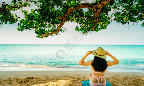 海滩穿着粉红泳衣和草帽放松在树下热带沙滩享受节假日暑时装的美女夏日时装感模特儿夏天情调时尚蓝色的背景图片