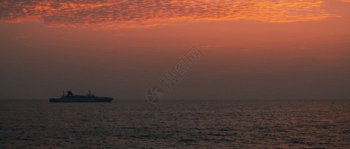 浪潮加勒一艘船在地平线上航行光辉多彩的日落天空平静低潮海滨冷静的图片