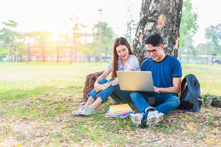 两个学生一起靠在树上看着电脑图片