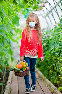 盛惠夏带着防面具的可爱小女孩在温室收获时间里盛满了蔬菜的大篮子在温室里收集黄瓜和番茄作物Cute小女孩在温室里收集黄瓜和番茄春天夏成熟背景