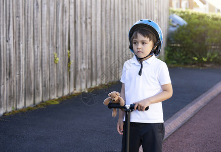 骑乐无穷儿童身着安全头盔骑滚车带着泰迪熊站的小孩看深思熟虑为儿童积极休闲和户外运动等活c儿童快速地乐的玩背景