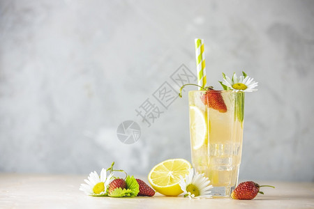 食物浆果用柠檬和草莓的冰冷清饮料玻璃杯装满柠檬和草莓在浅粉桌上供应新鲜鸡尾酒加冰果草药和甘菊装饰品眼镜背景图片