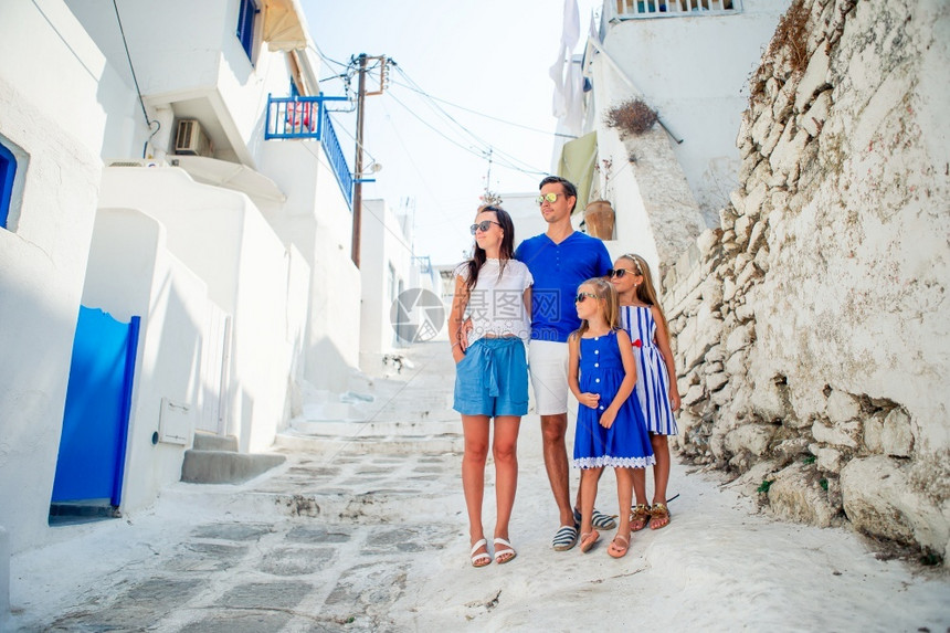 夏天父母和孩子在希腊Mykonos岛的典型希腊传统村庄街上度假在Mykonos岛有白色墙壁与多彩门家庭在Mykonos街上玩户外图片