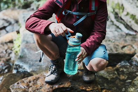 女人在爬山时用绿色水瓶装河流里的水图片