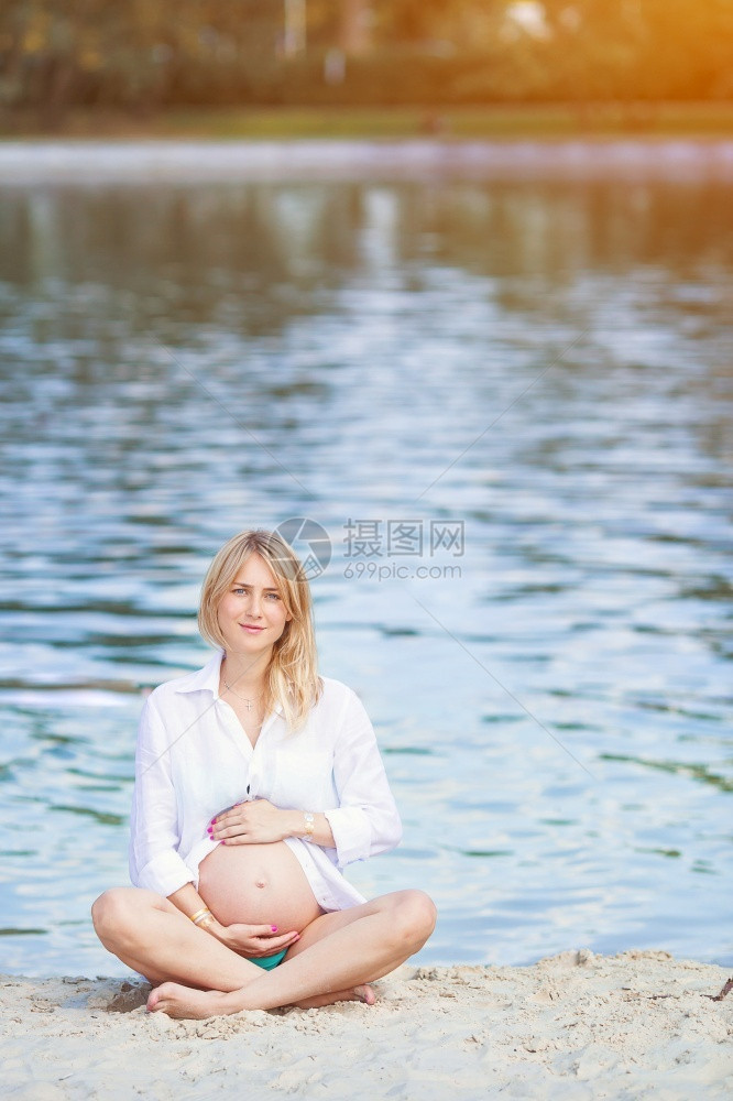 积极的超过金发女郎身在湖边莲花位置的怀孕美丽年轻妇放松了妊娠概念怀孕女孩穿着白衬衫阳光明媚的暑夏日背景在户外公园温暖天气的孕妇图片