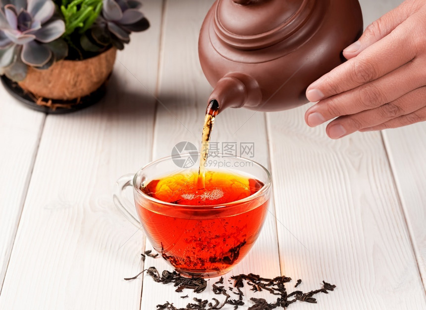混合泡茶的过程仪式从一个粘土茶壶红被倒入一杯玻璃新鲜酿成的黑茶温暖柔软灯光白木背景密闭抽烟光束图片
