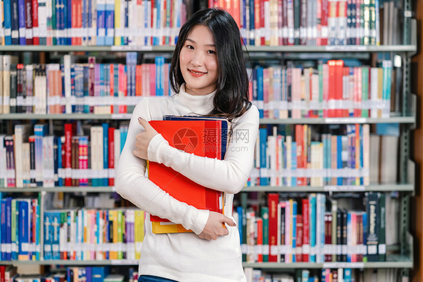 抱着书站在书架前的女学生图片