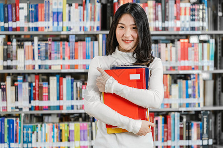 抱着书站在书架前的女青年图片