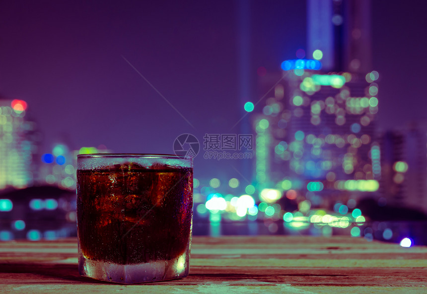 非酒精一杯碳化软饮料或可乐加冰和夜观博基城市的灯光紫色和黄音调图像模糊木制的图片