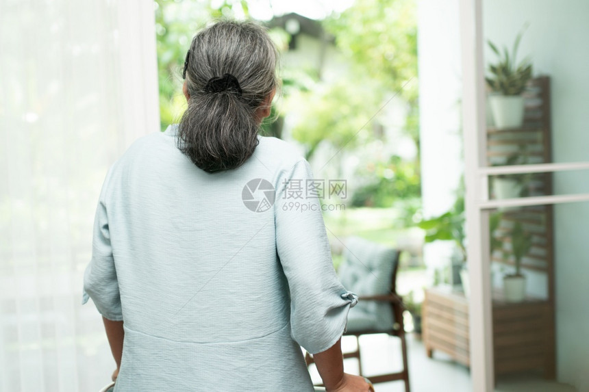 退休忧虑一位悲伤的年老妇女利用Walker站在窗户前看外感到孤单独她认为疾病和老年人照顾者造成的抑郁症概念一名可怜的老年妇女利用图片