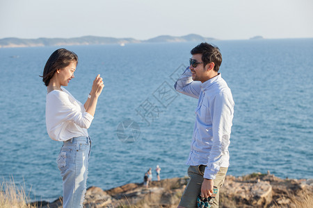 场地男人移动电话情侣放松绪在海边用智能电话拍照笑声图片
