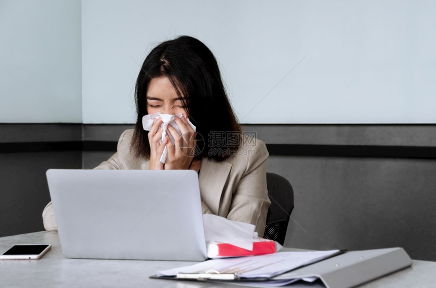 感染在会议室工作时坐在办公桌用膝上型电脑打喷嚏和在面部组织咳嗽的生病女司机在会议室工作时场所传播可乐的风险和Corona共食19图片