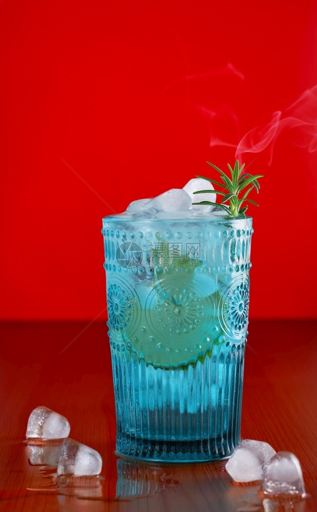 凉爽的柠檬汽水喝金银和调酒精饮料加石灰迷迭香以及生锈桌上的冰明红色底蓝玻璃鼓风机烟雾在清新玫瑰树枝上升夏季饮料图片