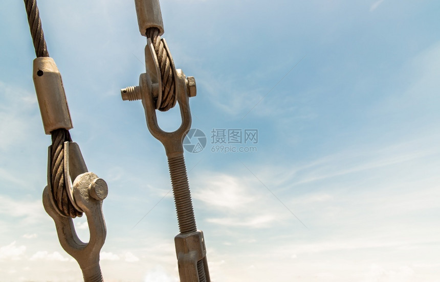 工业的固定安全钢交锁和螺旋键制钢或铁线绳索与螺栓连接的金属电缆夹以调整蓝色天空背景上电缆的紧张度或长设备连接概念和安全复制空间选图片