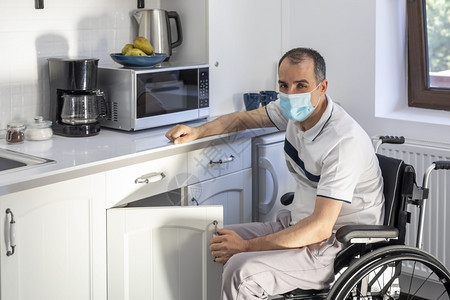 面肌瘫痪屋坐在轮椅上笑年轻残疾人在厨房门口面戴罩的青年男子他脸被聚焦在点上禁用传染背景