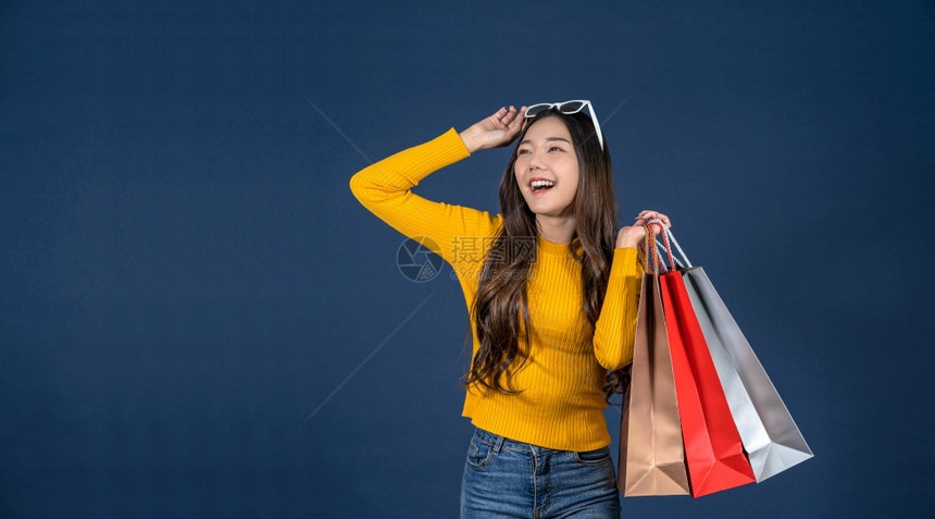 成功的自信带着一个以经典蓝肤色背景令人兴奋的购物袋销售折扣黑色星期五和消费主义概念夏季时装丰体等令人兴奋的东西笑着亚洲快乐的年轻图片