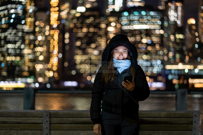 布鲁克林城市的幸福穿着冬季西装的亚洲女使用智能手机与微笑动作在东河背景美国市中心的纽约城风景照片上模糊的相布基赫Bokoh旁边图片
