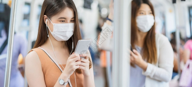 泰国轻轨地铁城市的通勤保护在Covid19爆发感染和大流行病概念的都市旅行时身戴外科面具并通过地铁火车智能手机监听音乐的亚洲女青年乘客在Co背景