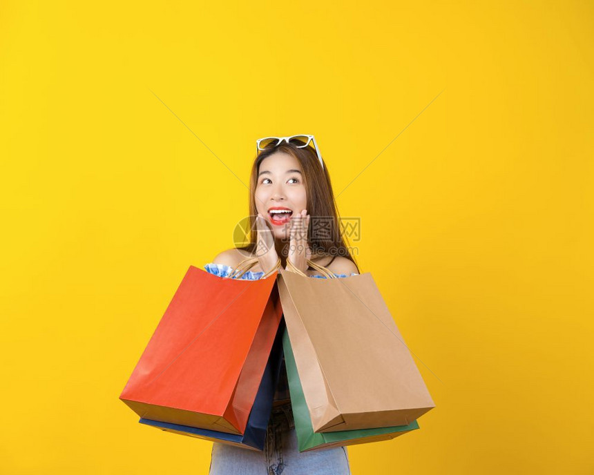 黄色背景前一名女性高兴点拿着多个购物袋图片
