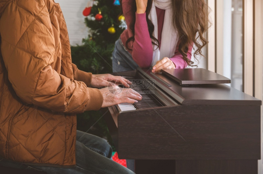 盛大两人在客厅享受愉快的时光与钢琴男一起弹为妇女唱歌在家里庆祝冬季节日她们在家一起庆祝冬季节日窗户女士图片