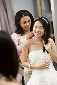 朋友帮助新娘微笑女性婚礼戏服镜子服装裙子反射女士服饰背景图片
