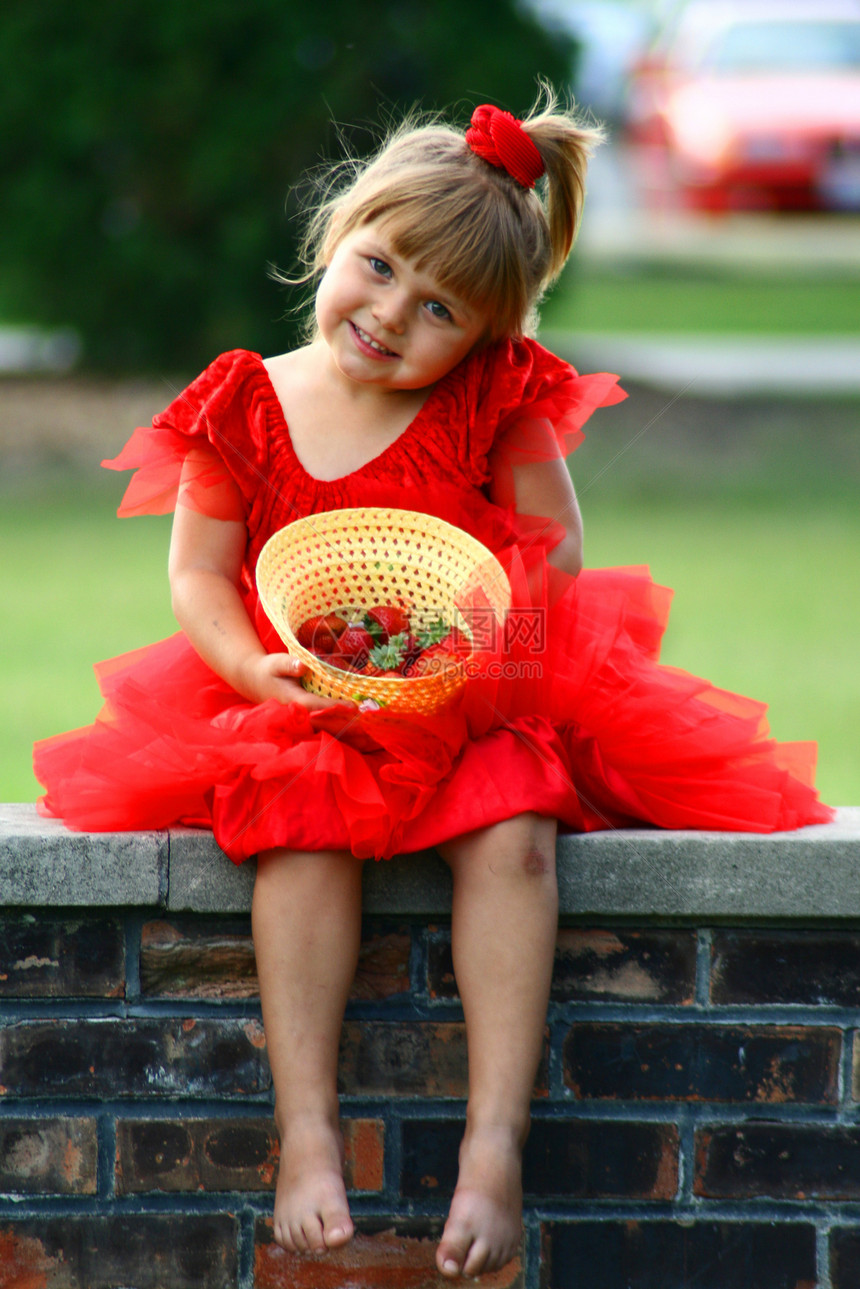 三岁女孩穿红衣坐在砖墙上 帽子里戴着草莓的图片