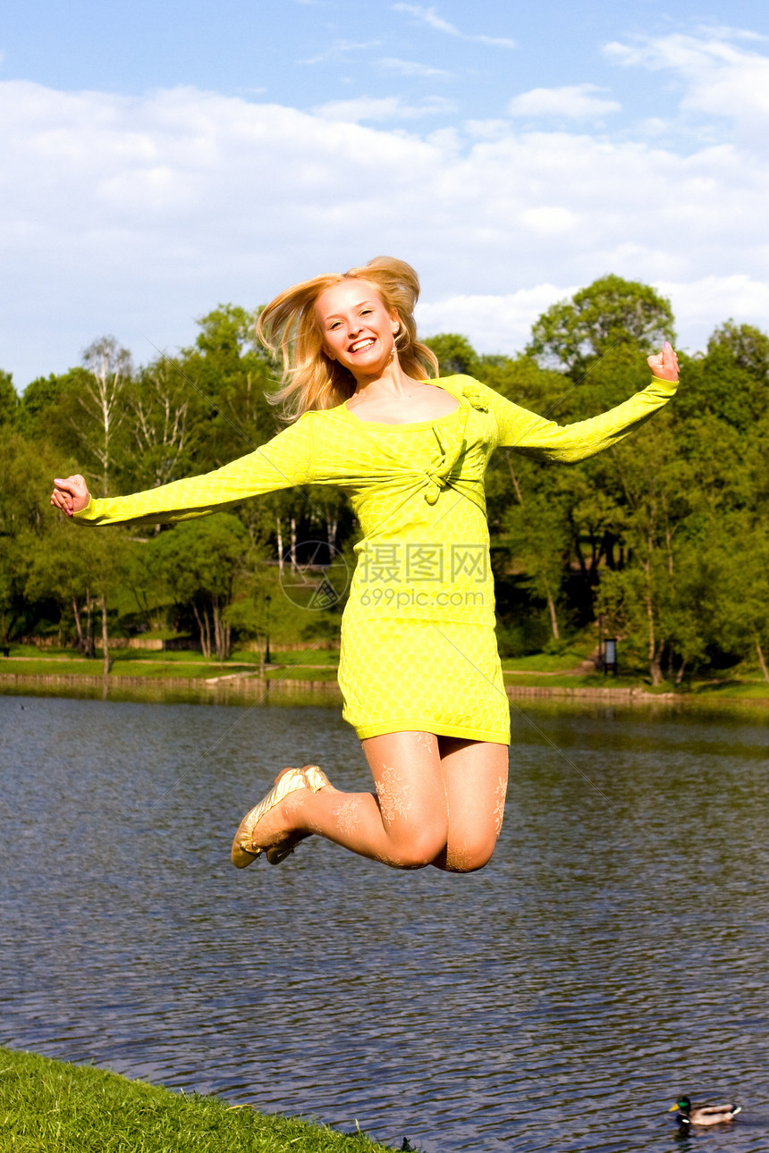 快乐的姑娘跳到河岸上闲暇女性微笑空气天空女士乐趣蓝色运动员幸福图片