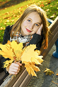 抓住叶子的女孩秋天的少女晴天微笑孩子们女性公园树叶叶子地面橙子幸福背景