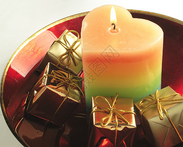红玻璃碗中的蜡烛和礼物反思条纹盒子盘子燃烧火焰红色心形背景图片