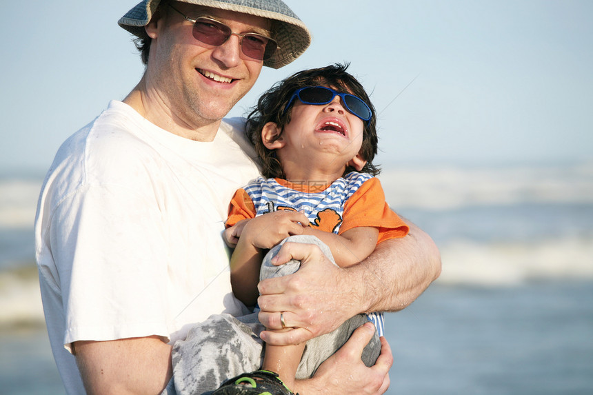 父亲在海滩上抱着哭着孩子的父亲图片